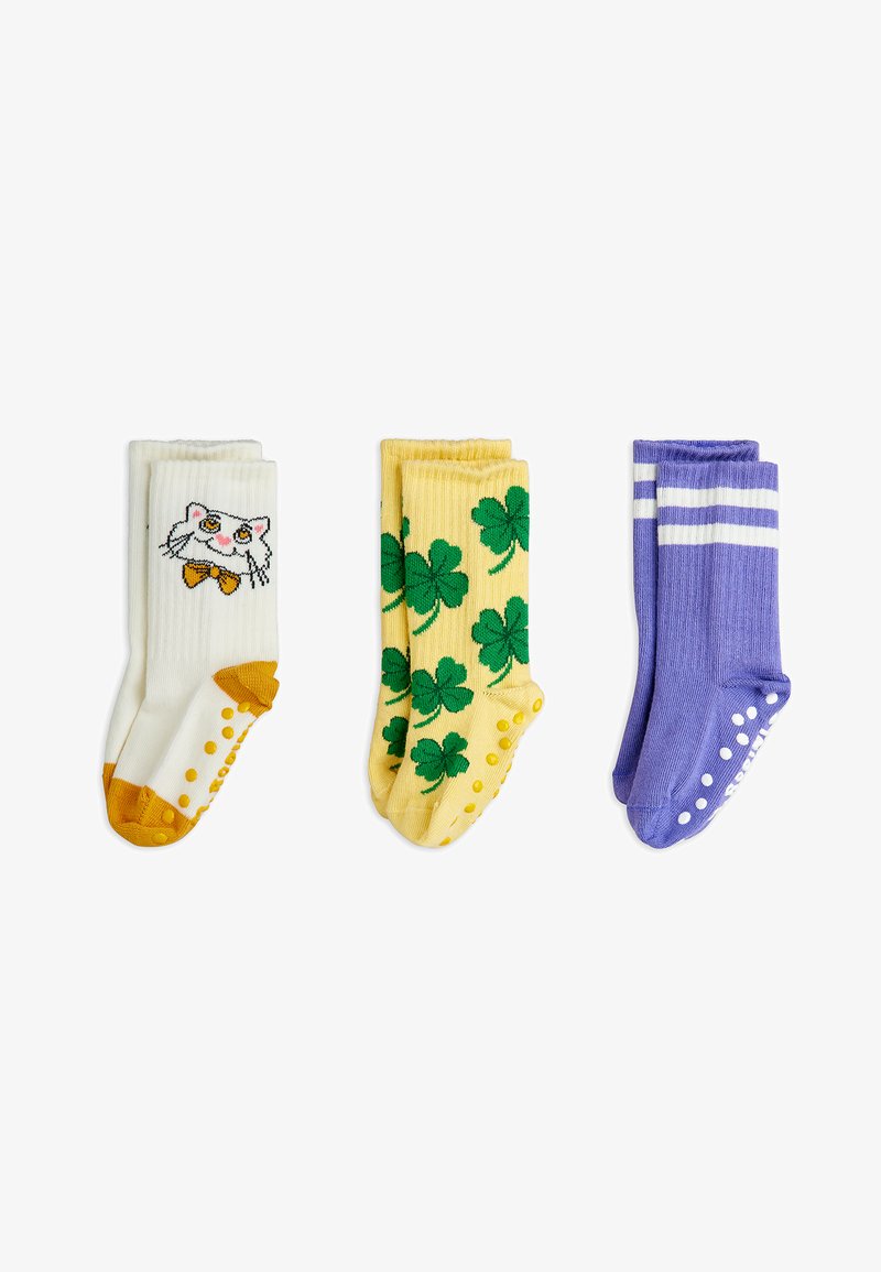 Tres pares de calcetines: blancos con diseño de gatos y acentos amarillos, amarillos con patrones de trébol verde, y morados con rayas blancas y antideslizantes.