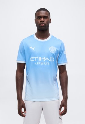 Férfi sportoló világoskék Manchester City labdarúgómezben, Etihad Airways logóval és fehér rövidnadrágban, szemben áll.