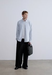 Svetlomodrý kardigán na gombíky cez svetlé tričko, v kombinácii s čiernymi širokými nohavicami a čiernymi topánkami. Drží čiernu koženú tašku.