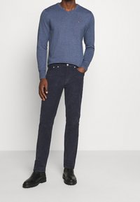 Granatowy sweter z dekoltem w serek, wykonany z miękkiego dzianego materiału, zestawiony z ciemnoniebieskimi spodniami ze sztruksu i czarnymi botkami za kostkę. Sweter zdobi subtelny detal z logo.