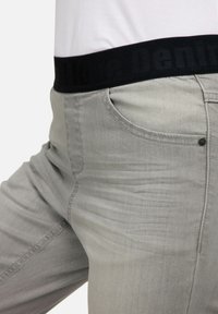 Jeans gris claro con una textura suave, que cuentan con una cinturilla elástica negra. Incluyen bolsillos frontales y detalles de costura a lo largo de las costuras.