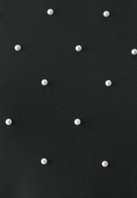 Svart strukturér tygtop med jämnt fördelade vita pärlaccent över ytan, vilket skapar en upphöjd mönster effekt.