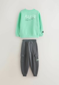 Mintgroene trui met tekstontwerp en grijze cargobroek met zakken. Beide gemaakt van zacht, comfortabel stof en hebben een ontspannen pasvorm.