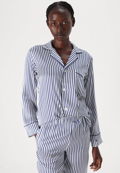 Dryžuotas pižamų komplektas baltoje ir tamsiai mėlynoje spalvose. Sudaro mygtukais užsegama marškinėlių su apykakle ir ilgomis rankovėmis, kelnių su elastine juosta ir kišenėmis komplektas.