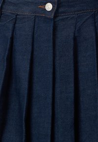 Fustă din denim bleumarin întunecat, cu pliuri, închidere cu nasture metalic și cusături portocalii contrastante. Textură netedă, cu un design clasic.