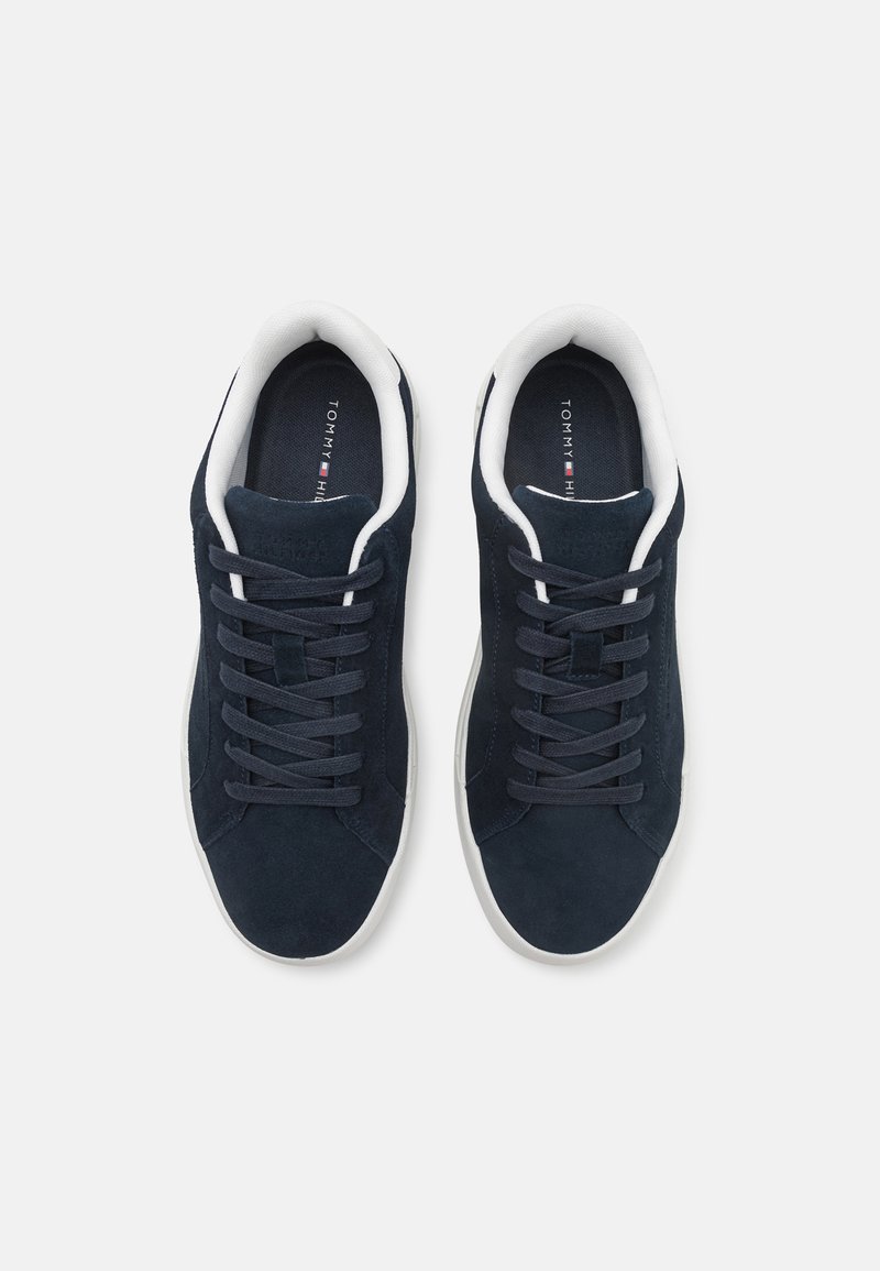 Baskets en suede bleu marine avec des accents blancs, lacets plats et une semelle texturée. L'intérieur présente un doublage doux et le logo de la marque sur la semelle intérieure.