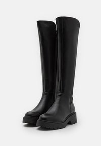 Bottes en cuir noires jusqu'aux genoux avec une texture lisse, une fermeture à glissière latérale proéminente, une semelle épaisse et un design à bout arrondi.