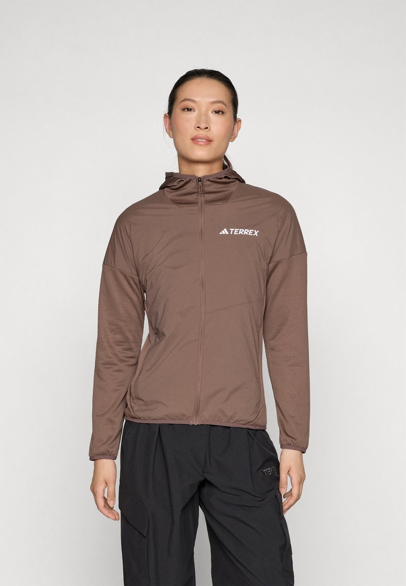 Giacca marrone con zip e cappuccio, realizzata in materiale leggero e testurizzato. Presenta il logo "Terrex" sul lato superiore destro.