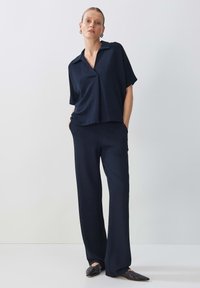 Chemise bleu marine à manches courtes avec col, assortie à un pantalon large en tissu lisse. Les deux présentent une coupe décontractée et un design minimaliste.