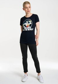 Černé tričko s grafickým designem zobrazujícím Wonder Woman a textem "Holky zachrání svět!" Ve slim-fit stylu, spárované s tmavými džíny.