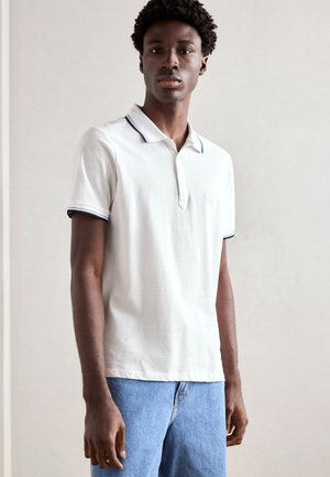 Polo shirt blanc avec un col classique, dotée d'accents bleu marine au niveau du col et des manches. Associée à un short en denim bleu clair.