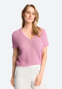 Kurzärmliger V-Ausschnitt Pullover aus hellrosa Strickmaterial, mit einem strukturierten Muster und lockerer Passform. Kombiniert mit hellen Hosen.