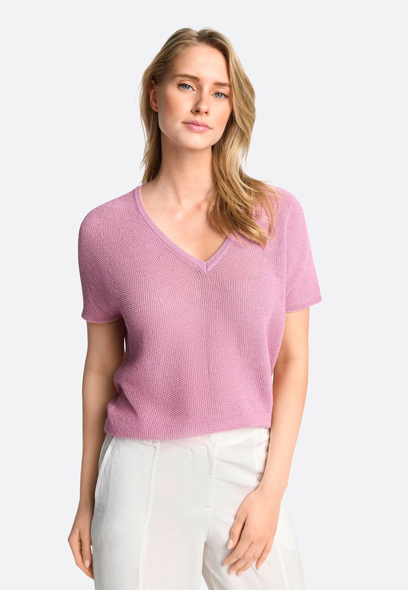 Kurzärmliger V-Ausschnitt Pullover aus hellrosa Strickmaterial, mit einem strukturierten Muster und lockerer Passform. Kombiniert mit hellen Hosen.