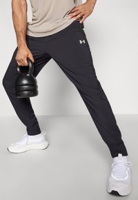 Μαύρο αθλητικό παντελόνι με στενή γραμμή, κατασκευασμένο από ελαφρύ ύφασμα, με λευκό λογότυπο στην αριστερή πλευρά και άψογη σχεδίαση χωρίς ραφές.