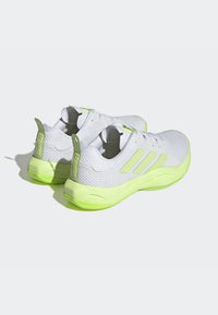 Weiße Sportschuhe mit einem Obermaterial aus Netzgewebe, leuchtend grünen Akzenten, strukturiertem Sohlenprofil und einem Fersenband, das mit "TRAINING" beschriftet ist. Glattes, leichtes Design.
