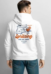 White hoodie featuring a cartoon alligator holding a cocktail. Text reads "Spritzing THE DAY AWAY" with light blue and orange accents.