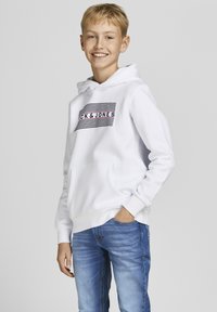 Felpa bianca con cappuccio, dotata di tasca frontale e grafica a righe orizzontali blu e rosse. Abbinata a jeans blu.