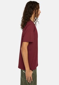 Burgunderfarbenes T-Shirt mit kurzen Ärmeln aus Baumwolle, das eine lockere Passform und einen Rundhalsausschnitt hat, kombiniert mit olivgrünen Hosen.