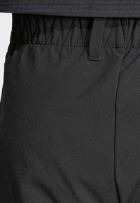 Černé sportovní kalhoty s texturovanou tkaninou, elastickým pasem a detailem švy, které mají hladký a flexibilní vzhled.