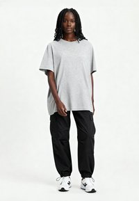Jasnoszary t-shirt z krótkim rękawem w połączeniu z czarnymi spodniami cargo. Spodnie mają elastyczne mankiety i kieszenie. Model nosi białe sneakersy.