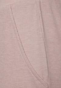 Pink ribbed fabric with a soft texture, featuring a side pocket and visible stitching detail. The design is simple and functional.