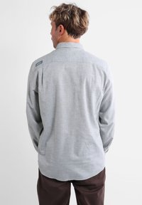 Chemise à manches longues pour hommes en tissu gris clair avec une texture lisse. Dotée d'un col classique et d'un détail de logo subtil sur l'épaule.