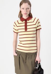 Gulstripete polo skjorte med røde striper og krage, med korte ermer og en placket med knapper. Bært med olivengrønne shorts.