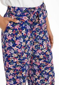 Spodnie kwiatowe z niebieskim tłem oraz intensywnymi różowymi, białymi i fioletowymi kwiatami. Posiadają związaną talię i boczne kieszenie dla większej funkcjonalności.