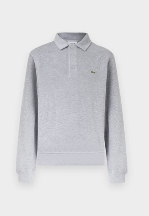 Hellgraues Poloshirt mit langen Ärmeln, gerippten Bündchen, drei Knöpfen am Kragen und einem kleinen grünen Krokodil-Logo auf der linken Brust.