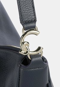 Blauwe leren handtas met een gestructureerd oppervlak, voorzien van een glanzend gouden logo hardware detail op de band en een ritssluiting.