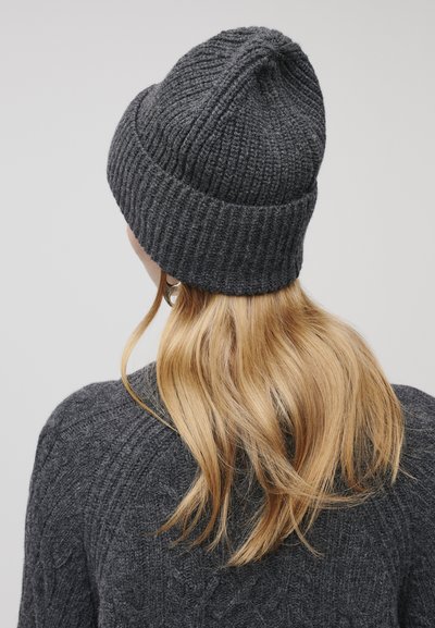 Berretto in maglia grigia con texture a coste e risvolto. Materiale in misto lana. La vista posteriore mostra capelli sciolti che cadono su un maglione scuro.