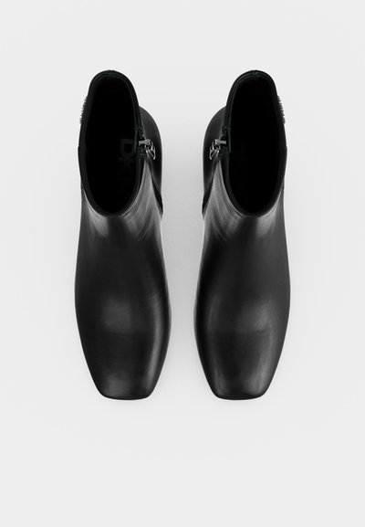 Paire de bottines noires en cuir avec bouts carrés et fermetures éclair latérales, vues de dessus sur fond blanc.