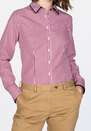 Camisa de botones a cuadros rojos y blancos con cuello, ribete azul marino contrastante y mangas largas, combinada con pantalones beige.