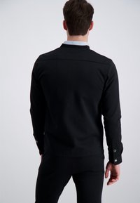 Czarna koszula z długim rękawem, o prostym kroju i teksturowanej tkaninie. Posiada mankiety na guziki i kontrastujący kołnierz. Gładki, minimalistyczny design.