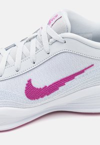 Hvid Nike sko med en struktureret strikoverdel, pink broderet swoosh, hvide snørebånd og gummisål med pink detalje.