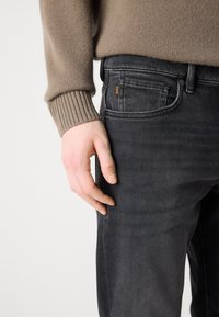 Gray denim jeans with a slim fit, featuring a front pocket and discreet logo detail. Pairing with a beige knit sweater.