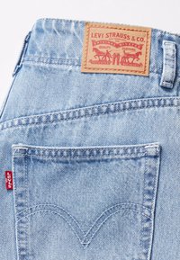 Ljusblå denimjeans med en strukturerad yta, som har en brun läderlabel och en röd Levi's-tag på bakfickan.