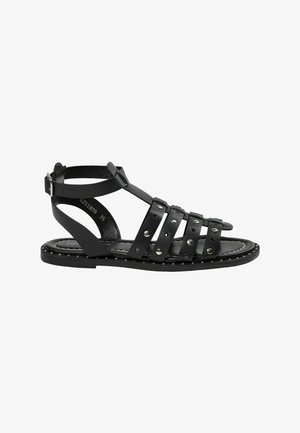 Sandale gladiateur noire plate avec bride à la cheville, plusieurs brides horizontales avec des clous argentés et fermeture par boucle.