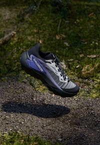 Běžecká obuv na trail s černou a šedou síťovinou a fialovými akcenty. Lehký design s texturovanou podrážkou pro přilnavost.