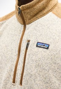 Μπεζ και καφέ fleece μπουφάν Patagonia με δύο καφέ φερμουάρ, ένα στο στήθος και ένα που τρέχει από το γιακά μέχρι το μέσο του στήθους, δείχνοντας την υφή του υφάσματος.