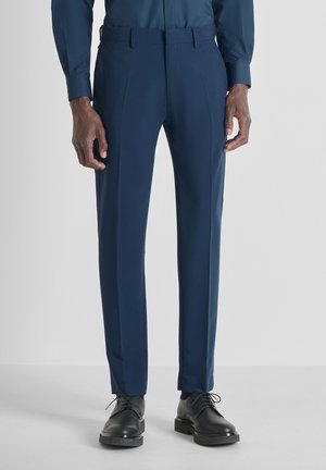 Pantaloni tailored blu navy in tessuto liscio, con taglio dritto, tasche laterali e cuciture eleganti, abbinati a scarpe nere.