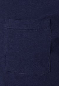 Țesătură din bumbac bleu marin cu o suprafață texturată, prezentând o buzunar cusut cu grijă pe partea stângă, de formă rectangulară.