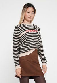 Gestreifter Pullover in Schwarz und Beige mit "J'ADORE" in Rot, aus weichem Material. Kombiniert mit einem braunen Rock, der einen mehrschichtigen Look kreiert.