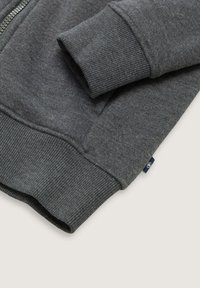 Gray sweatshirt featuring a textured fabric, ribbed cuffs and hem, with a front zipper and a small logo patch on the side.