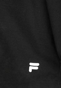 Tessuto in cotone nero con logo bianco "F". La vista ravvicinata evidenzia la superficie texturizzata e i dettagli delle cuciture.