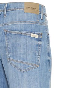 Hellblaue Jeans aus Denim mit sichtbarer Gesäßtasche, Lederetikett an der Taille und dekorativen Stickdetails.