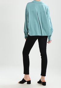 Blusa de manga larga en azul claro con cuello y puños abotonados, combinada con pantalones skinny negros y sandalias de tacón cuadrado destalonadas.
