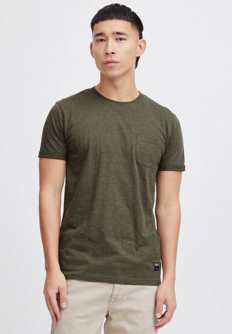 T-shirt olive en manches courtes avec un col rond, une poche poitrine et une étiquette en tissu en bas à gauche. Texture douce.
