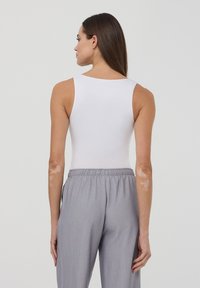Body bianco senza maniche con scollatura rotonda, abbinato a pantaloni grigi larghi con elastico in vita, visti da dietro.