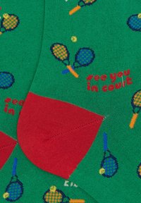 Calzini verdi con un motivo di racchette e palline da tennis, con un accento rosso nel tallone. Il testo recita "ci vediamo in campo."